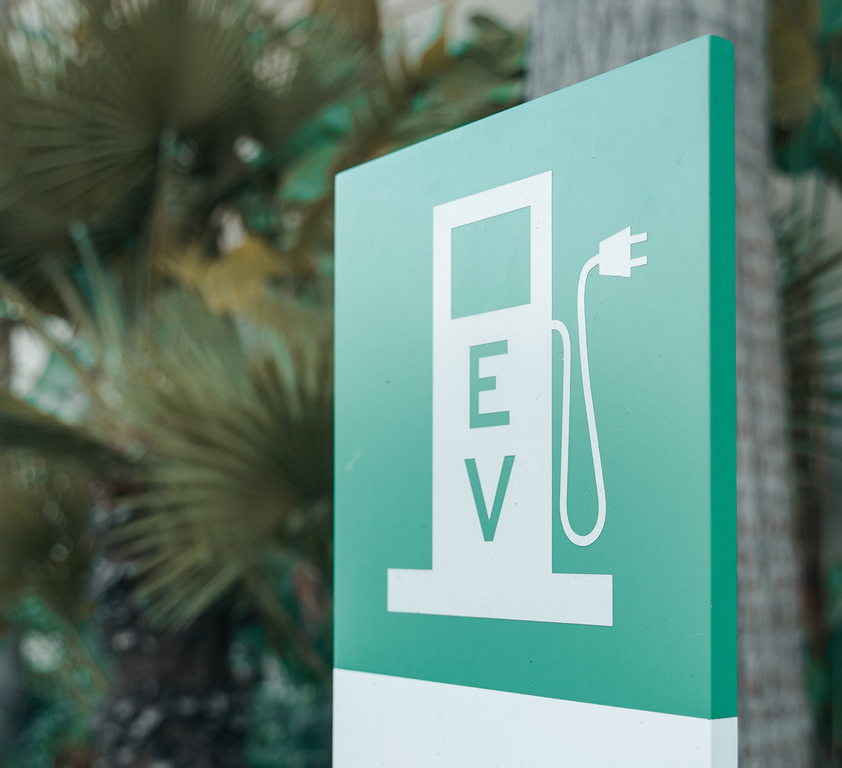 green EV charging station sign with jungle type foliage in the background